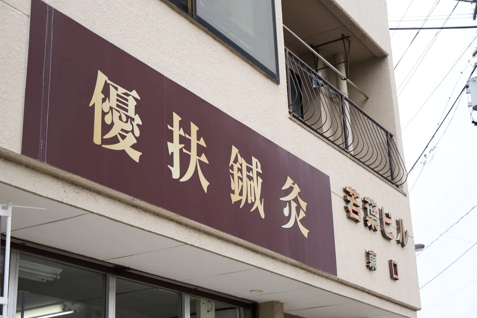 入口の上に掲げた「優扶鍼灸」の看板。建物名と入口の表示も並んでいる。