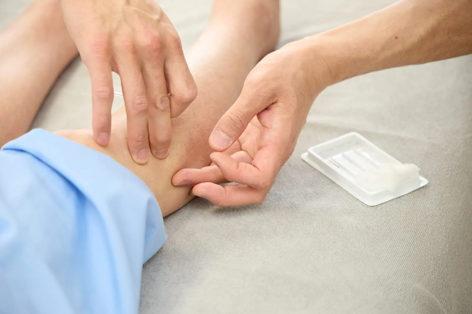 前腕に鍼を入れているところの手元。横に使い捨て鍼の個包装が置かれている。